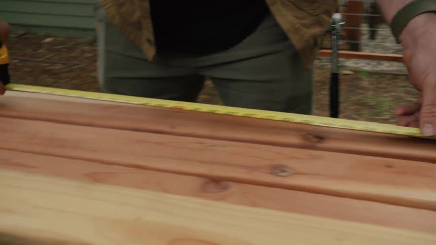 Close up slow motion shot of a man's hands measuring a piece of lumber with a tape measure in his backyard