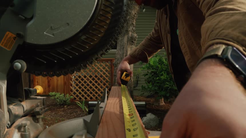 Close-up shot of a craftsman's hands carefully measuring a wooden plank with a tape measure on a miter saw