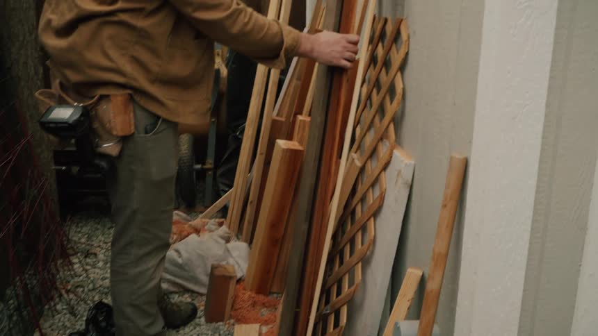 A carpenter sorts through a pile of various scrap lumber while preparing for a project in his backyard