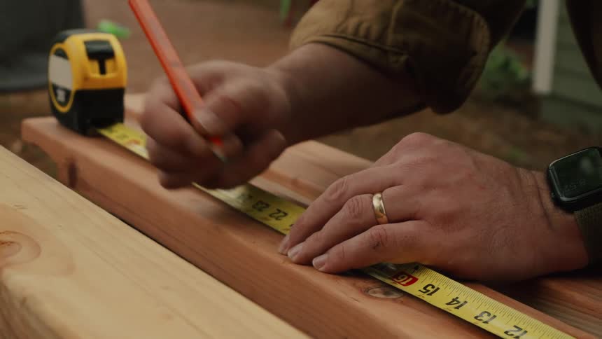 Close-up of a craftsman's hands measuring and marking a wooden board with a tape measure and pencil for a DIY project