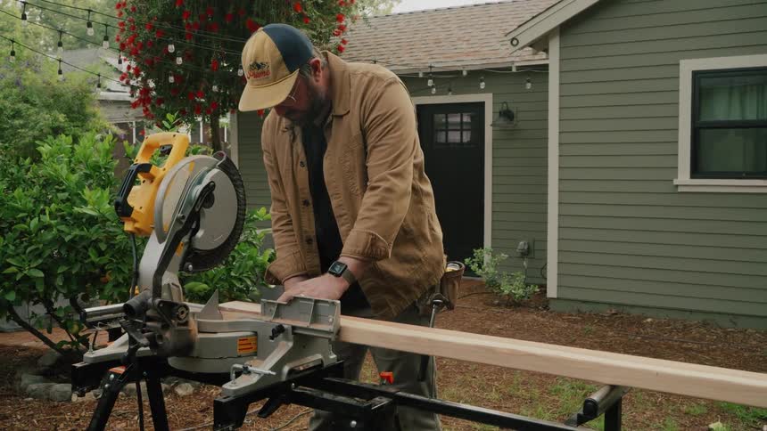 A skilled carpenter precisely operates a miter saw to cut a wooden beam in a residential backyard