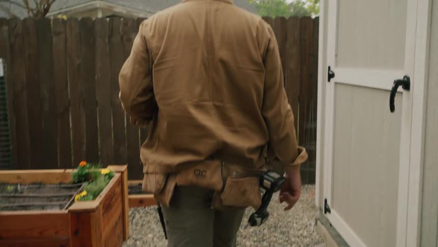 A handyman opens a new wooden gate and walks through a gravel path in a backyard garden