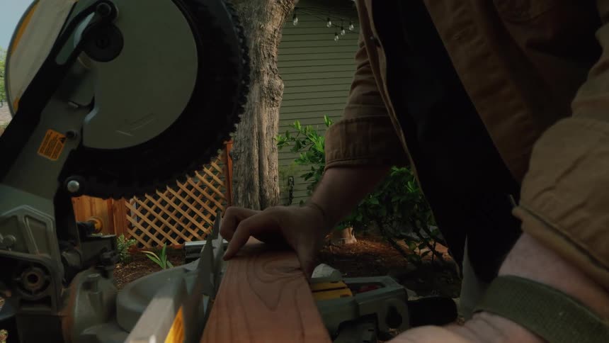 An over-the-shoulder slow-motion shot reveals a craftsman lining up a piece of wood on a miter saw before marking his cut