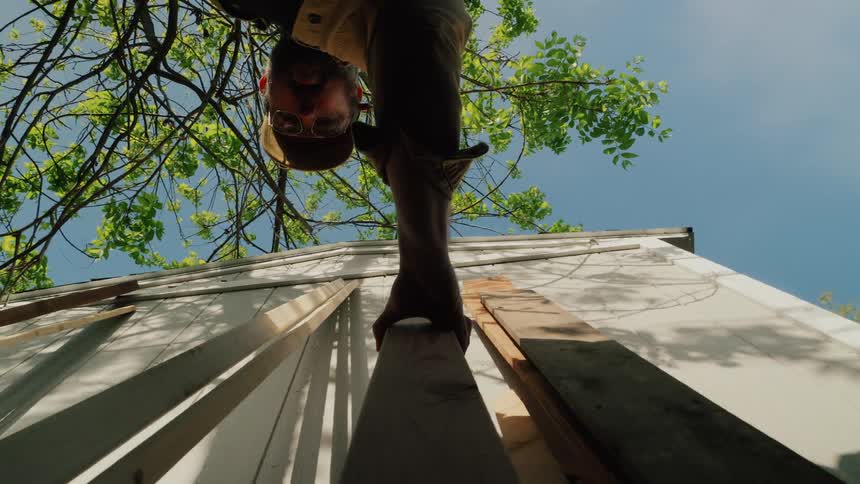 Unique low-angle point-of-view shot of a man measuring a wooden plank outdoors on a sunny day