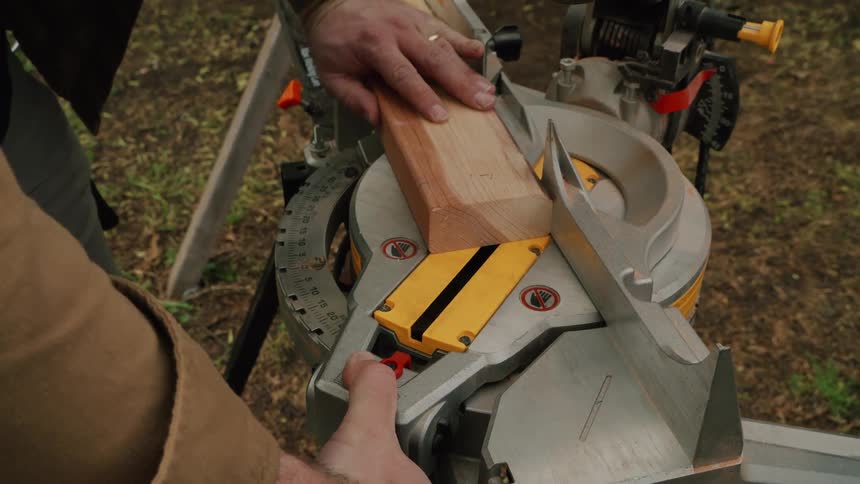A woodworker carefully adjusts the miter saw's angle before making a precise cut on a block of wood