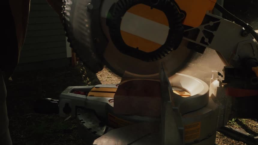 Close up slow motion of a powerful miter saw blade cutting through a block of wood, sending sawdust flying through the air