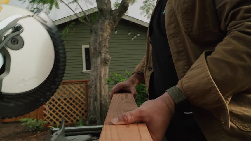 A slow-moving close-up shot of a woodworker's hands aligning a wooden plank on a miter saw in a backyard setting