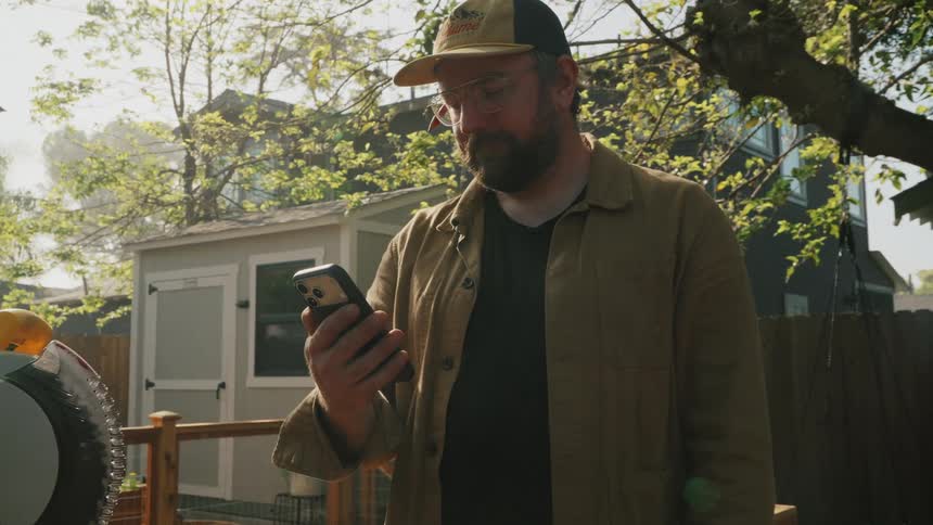 A man working on a project in his backyard stops to look at his phone