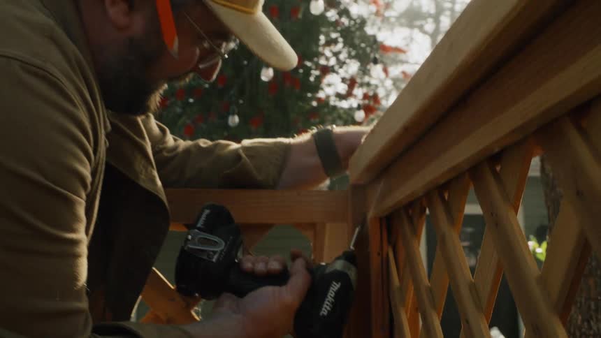 Slow-motion close-up of a man using a power drill to screw together a wooden lattice fence outdoors in the sun
