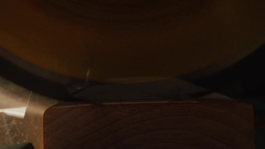 An extreme close-up of a miter saw blade cutting through a wooden board in slow motion, sending sawdust flying