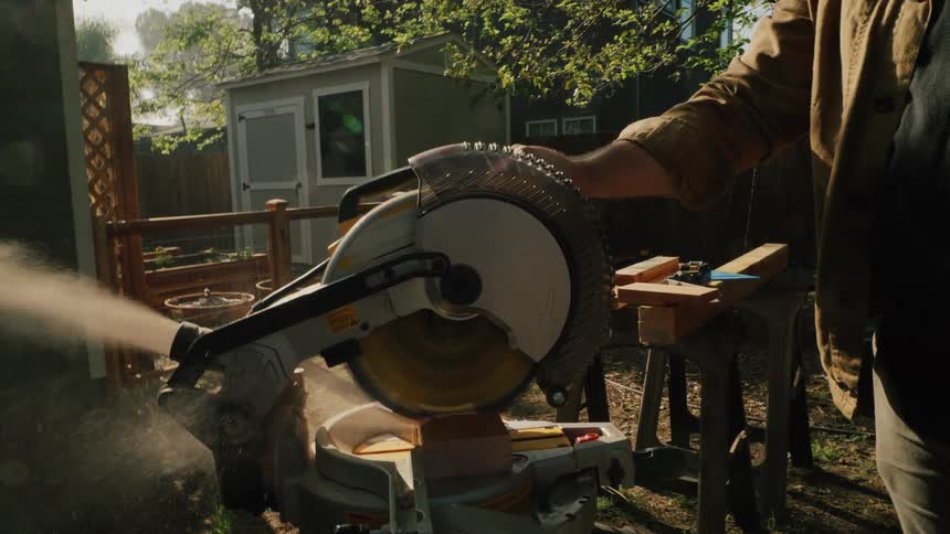 Slow motion vertical close-up of a circular saw cutting through a wooden board, with sawdust flying through the air on a sunny day