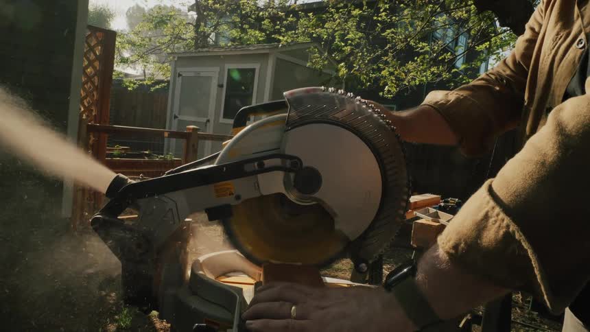 Vertical slow motion close-up of a woodworker cutting a piece of lumber with a miter saw in a sunny backyard