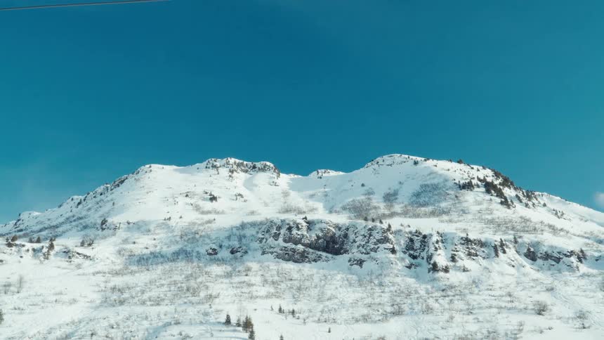 A slow pull-back aerial shot of a majestic snow-covered mountain range against a brilliant clear blue sky