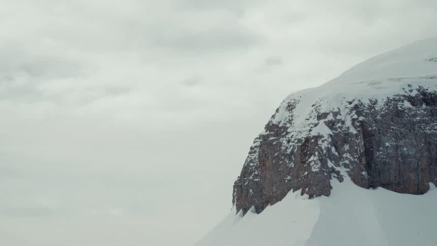 Static shot of a snow-covered mountain peak under a gray, overcast sky