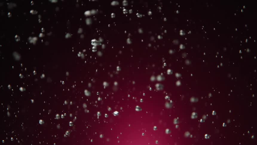 Slow motion close up of sparkling bubbles rising in liquid against a deep magenta background