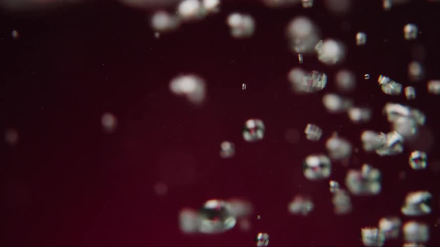 Abstract macro shot of shimmering bubbles rising in slow motion through a dark red liquid