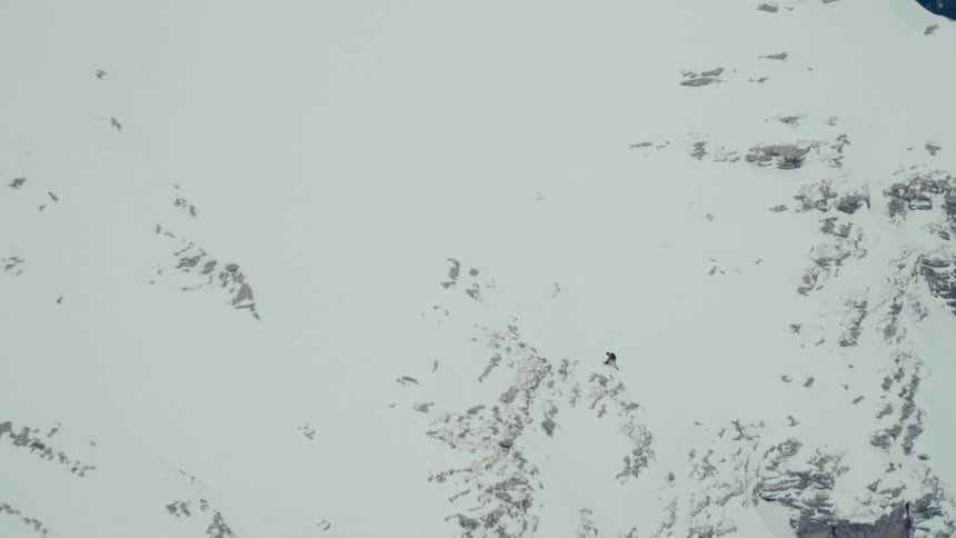 Wide shot of an extreme snowboarder descending a massive, rugged, snow-covered mountain