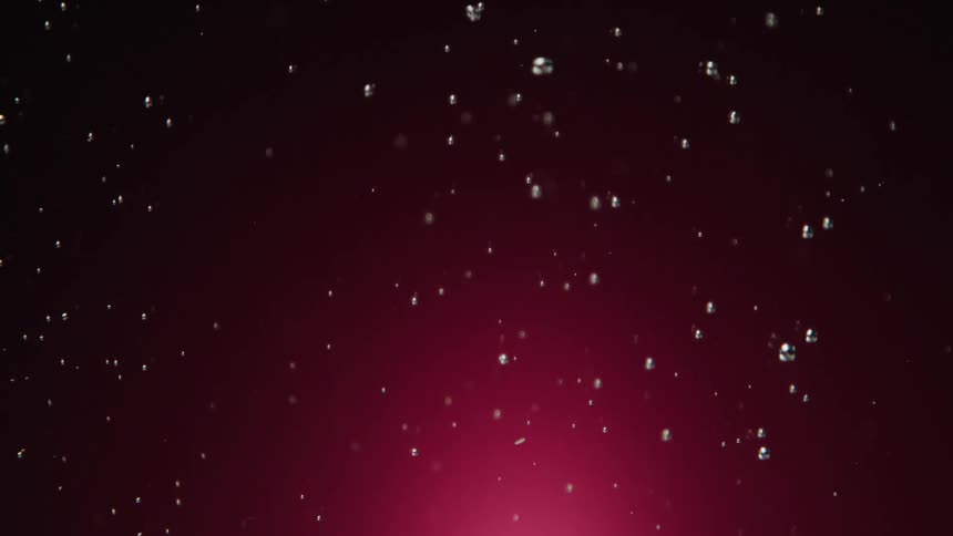 Shimmering water droplets dance and fall in slow motion against a dramatic magenta background
