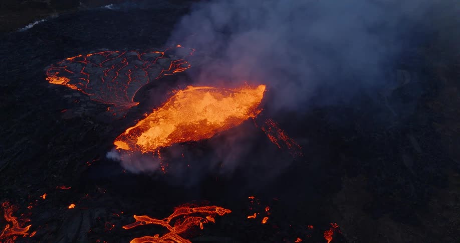 Powerful aerial footage captures the raw force of a volcano erupting at dusk, with its fiery crater contrasting against the dark, smoky landscape