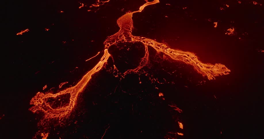 An aerial drone shot slowly pulls away from a mesmerizing river of molten orange lava flowing over dark volcanic rock