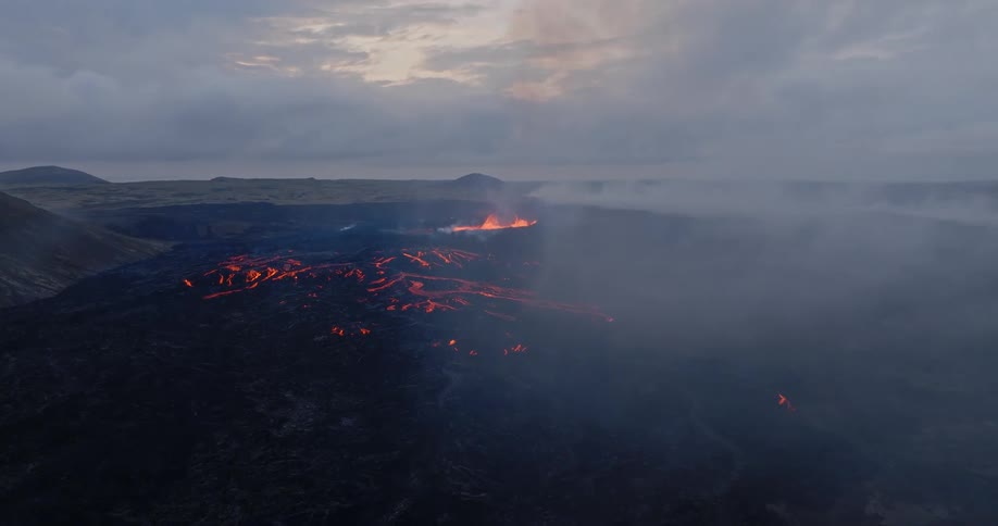 Dramatic aerial view of a smoldering volcano with fiery lava rivers and heavy smoke at twilight