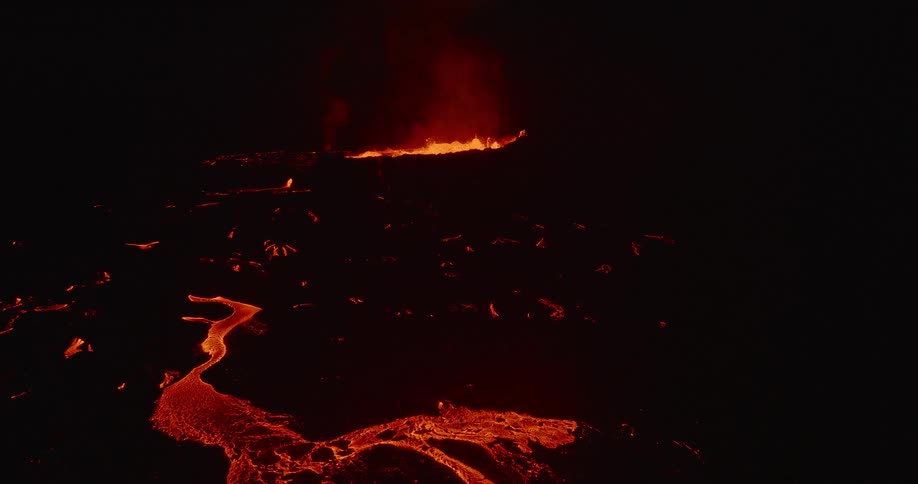 Fiery volcanic eruption illuminates the night sky as molten lava flows from the crater across a vast, dark field