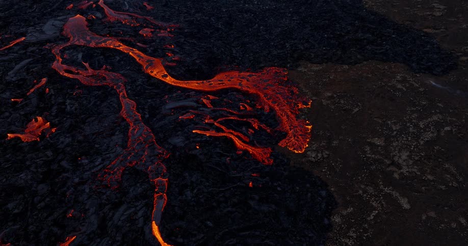 A dramatic aerial shot tilts down over a vast volcanic landscape, revealing rivers of red-hot lava flowing from an active eruption
