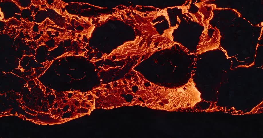 A top-down shot captures the mesmerizing flow of a molten lava river, with its fiery orange glow and cracking black crust