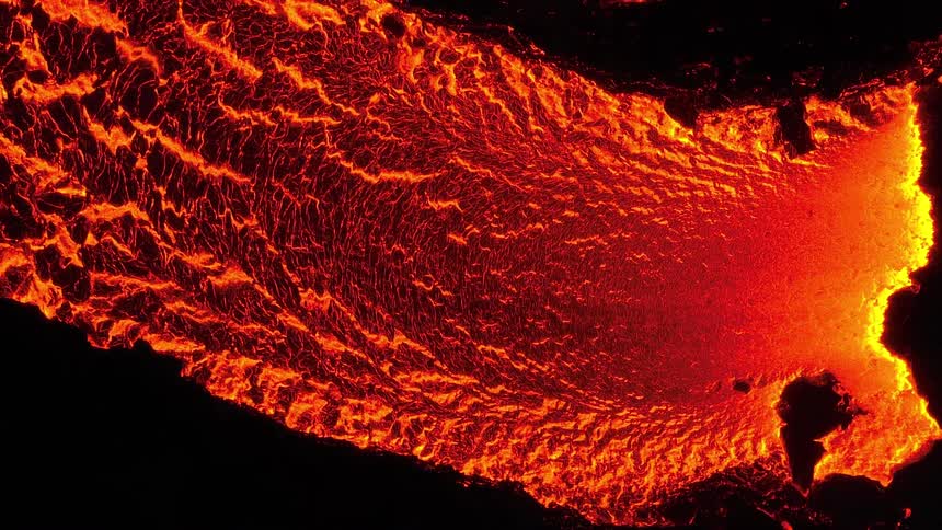 Mesmerizing aerial top-down view of a glowing red river of molten lava flowing and cracking