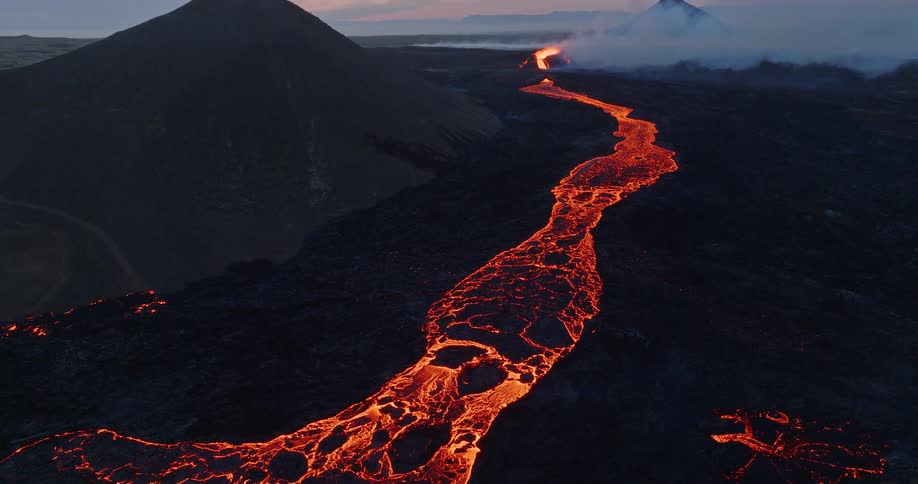 Stunning aerial view revealing a glowing river of molten lava flowing from an erupting volcano at dusk