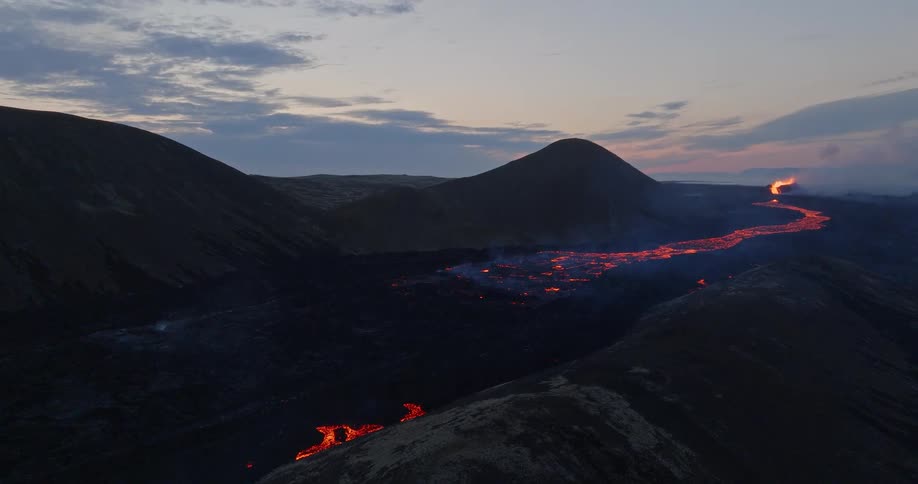 Stunning aerial ascent reveals a glowing river of molten lava flowing from a volcanic eruption through a desolate valley at dusk