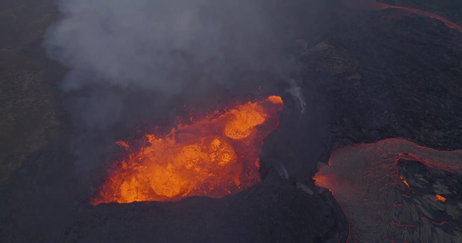 A dramatic top-down aerial shot slowly pulls away from a bubbling volcanic crater to reveal the vast, smoky landscape of the eruption site
