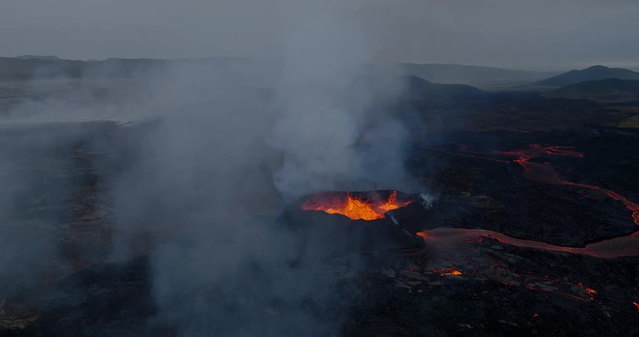 A dramatic aerial view captures the raw power of a volcano erupting, with molten lava flowing from its crater amidst thick clouds of smoke