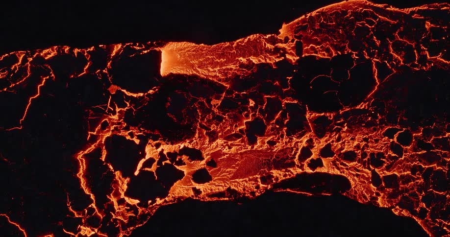 A mesmerizing top-down aerial shot shows a glowing river of molten lava slowly flowing and hardening into a dark, cracked crust
