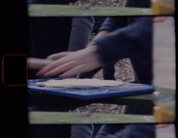 Vintage Super 8 film captures a close-up of hands using a rolling pin on dough outdoors