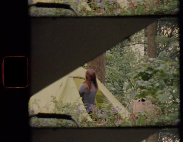 Super 8mm film shows a woman setting up her tent in a lush forest surrounded by bluebells