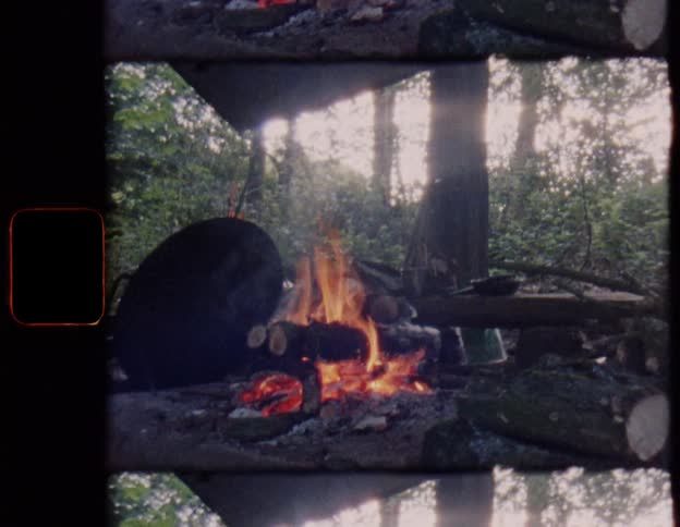 Nostalgic film captures a burning campfire with a cooking pot at a rustic campsite in the forest