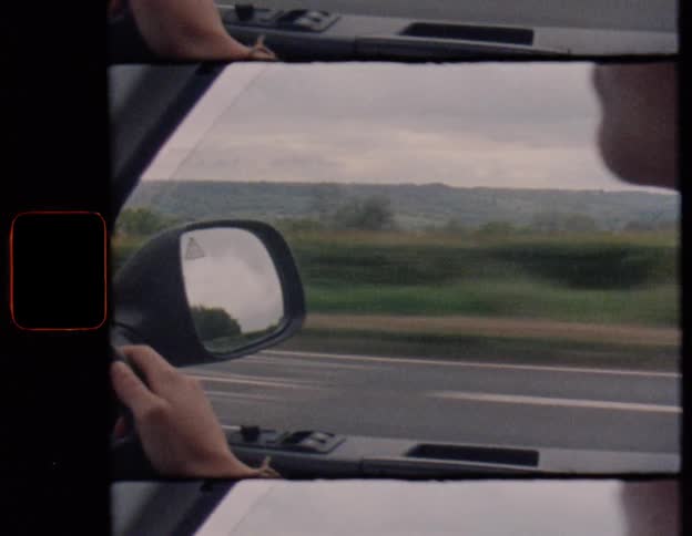 A person drives a car through the scenic countryside on an overcast day in this vintage film-style shot