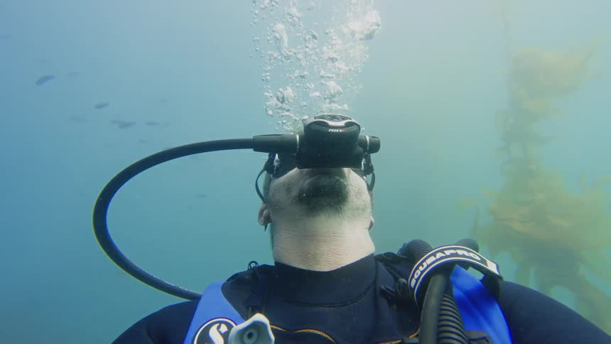 Slow motion selfie view of a scuba diver's face as he breathes through his regulator underwater