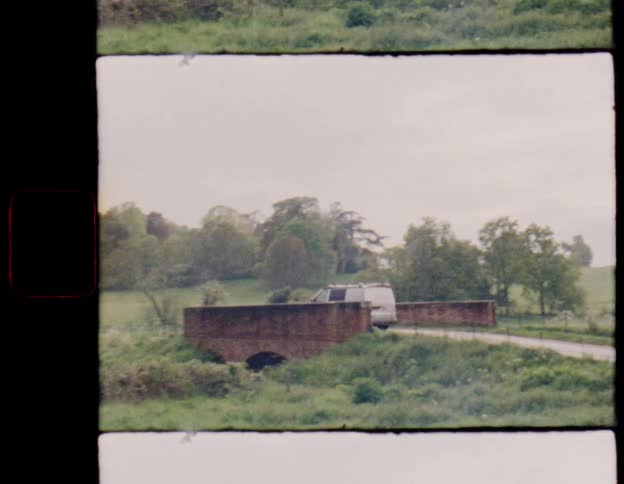 Authentic vintage film captures a van driving over a charming brick bridge in the picturesque green countryside