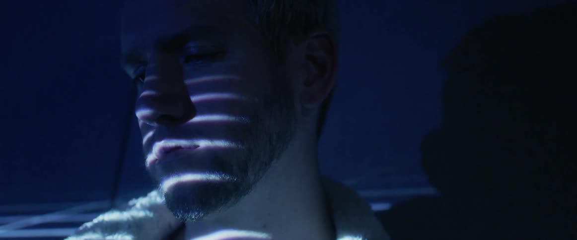 Lights shine onto a man's face in a dark room