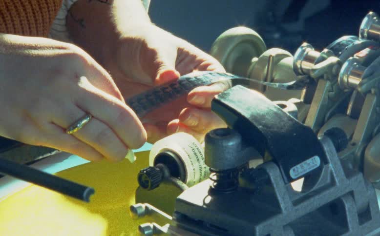 A film technician carefully cleans a strip of 16mm celluloid film by hand on an editing bench