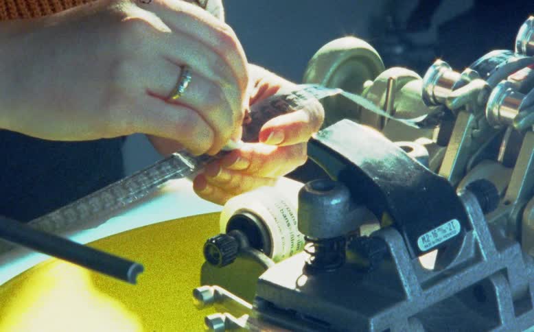 A close-up shot of a film editor's hands carefully cleaning a strip of analog film on a synchronizer machine