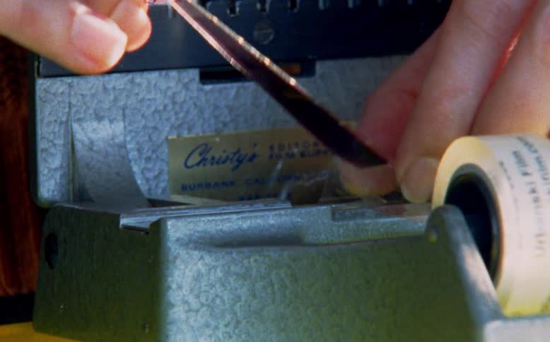 A close-up shot of a film editor's hands splicing together film using a vintage splicer and tape