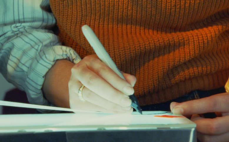 A person in a warm orange sweater draws with a black permanent marker on a lightbox