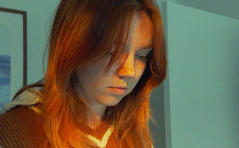 A peaceful young woman with red hair closes her eyes in the warm, golden glow of a quiet room