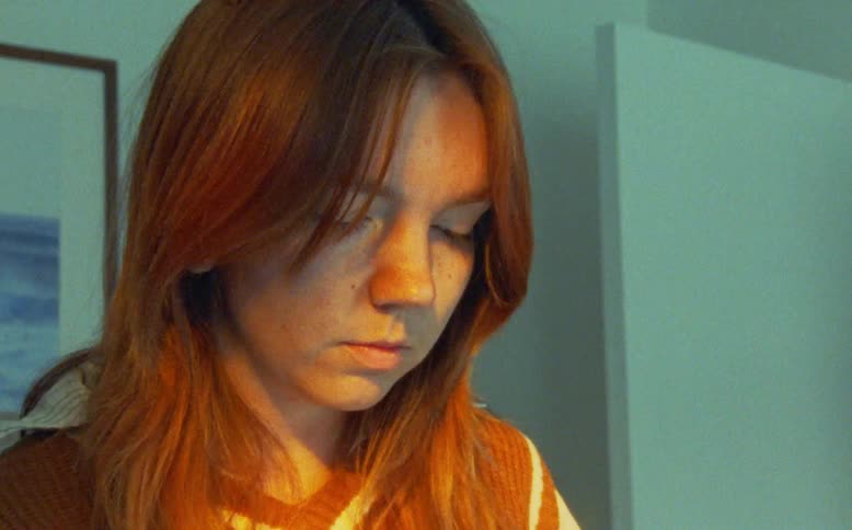 A thoughtful young woman with red hair looks down in a moment of quiet introspection