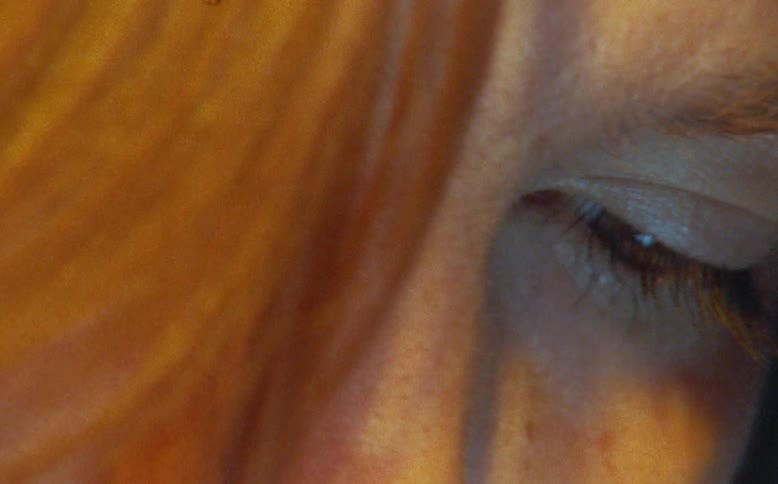 An extreme close-up of a woman's face, illuminated by warm, golden light, creating a pensive and introspective mood