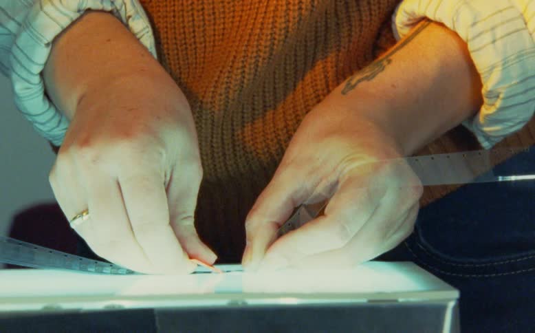 Close-up shot of a filmmaker's hands coloring a strip of celluloid film on a light table