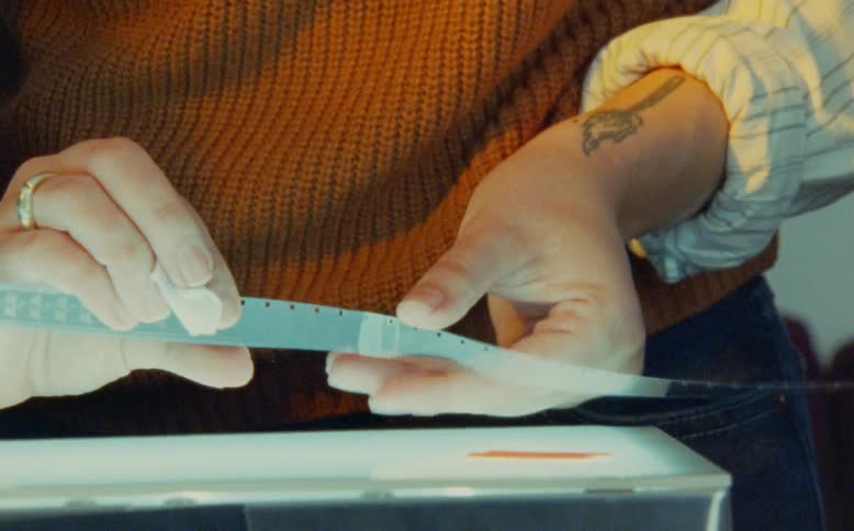 A filmmaker meticulously cleans a vintage 16mm film strip by hand on a professional light table